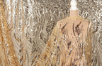 a mannequin wearing a gold and beige sequined dress with a sheer overlay.