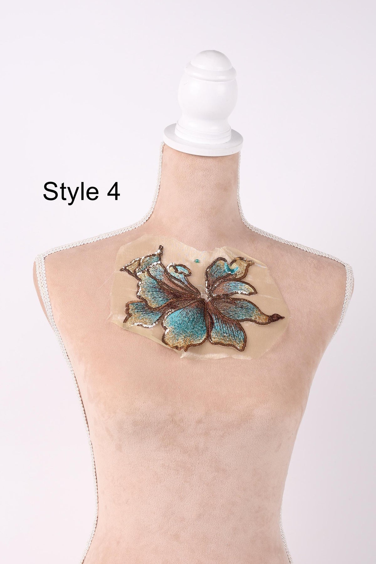 A mannequin with a beige body and a white headpiece, displaying a blue and green floral embroidered design on its chest.