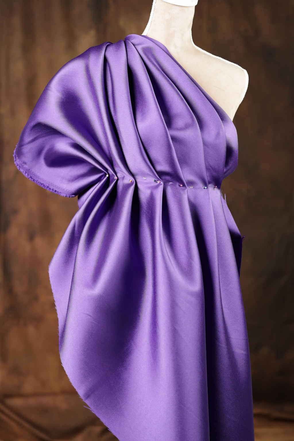 A close-up view of a purple satin fabric, possibly a dress or garment, with a ruched and pleated appearance.