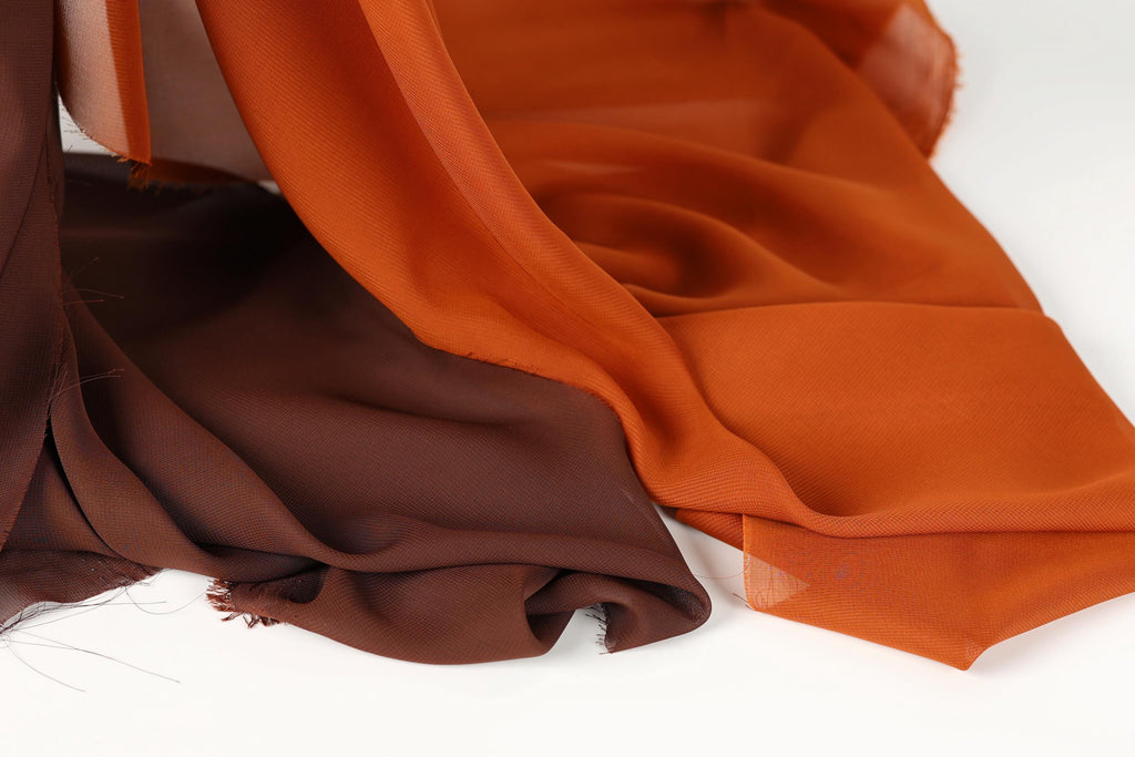 a close-up view of two fabric swatches, one in a dark brown color and the other in a bright orange color, both appearing to be made of chiffon or a similar type of fabric.