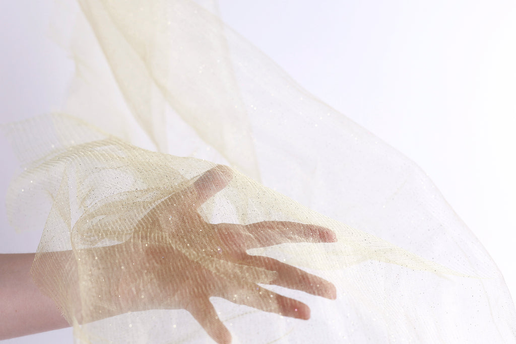 A hand is holding a piece of light yellow fabric, which appears to be a sheer or sheer-like material.