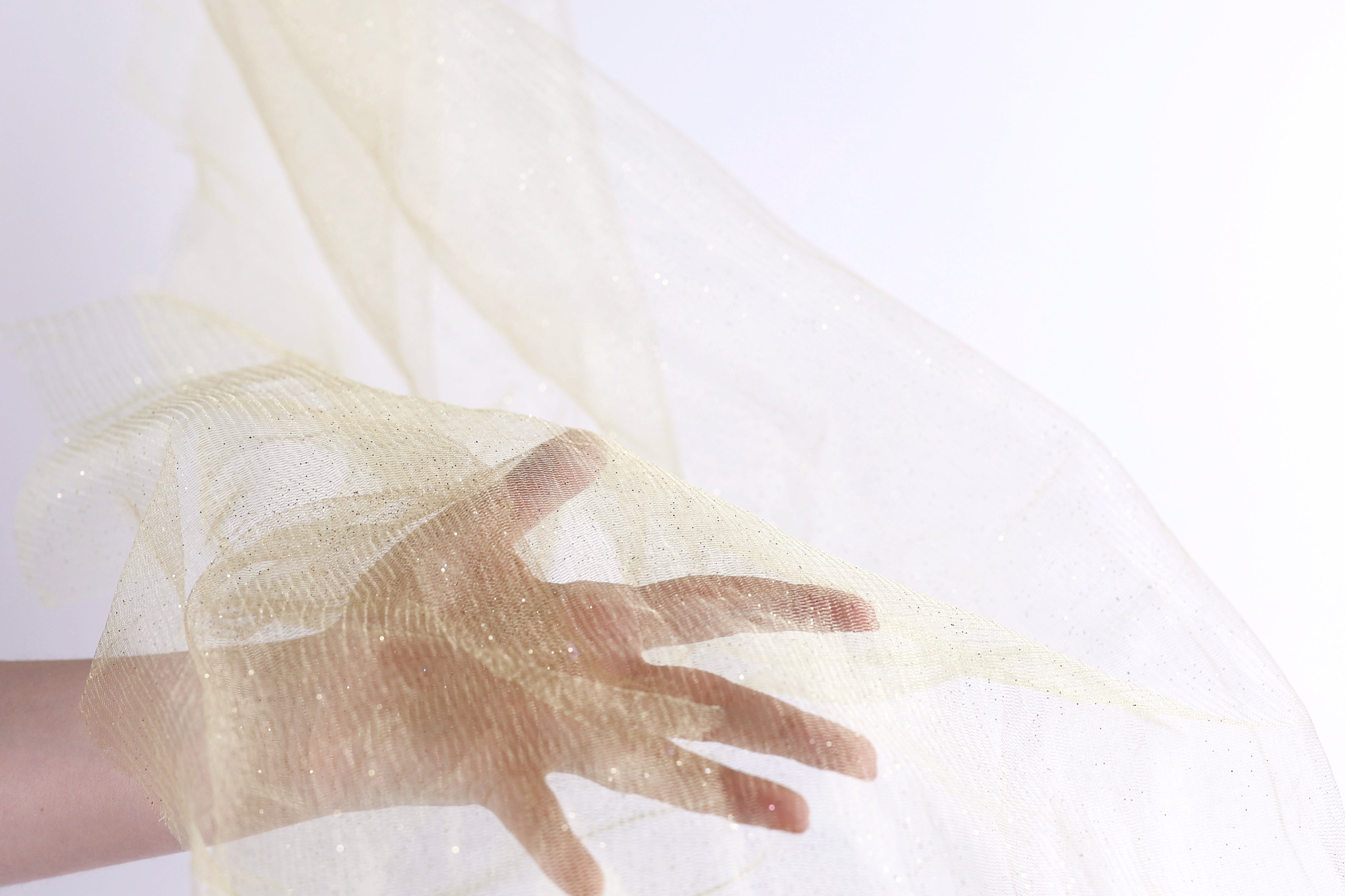 A hand is holding a piece of light yellow fabric, which appears to be a sheer or sheer-like material.