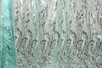 a close-up view of a fabric with a repeating pattern of green and black leaf-like designs. The pattern is intricate and detailed, creating a visually striking and textured appearance.