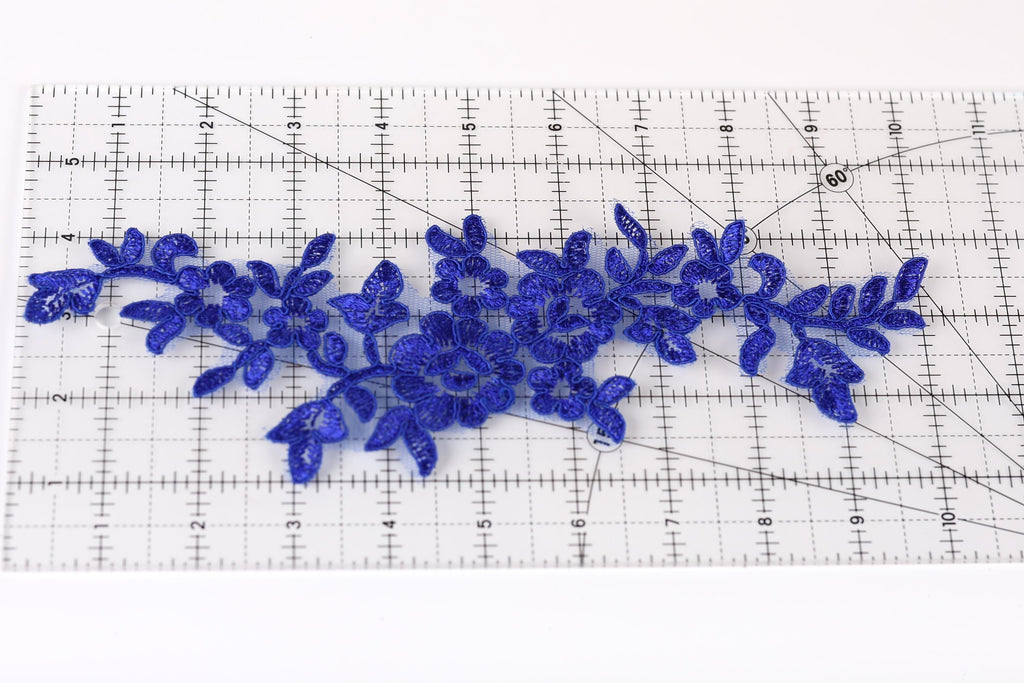 a close-up view of a clear ruler with blue floral embroidery pieces placed on it.