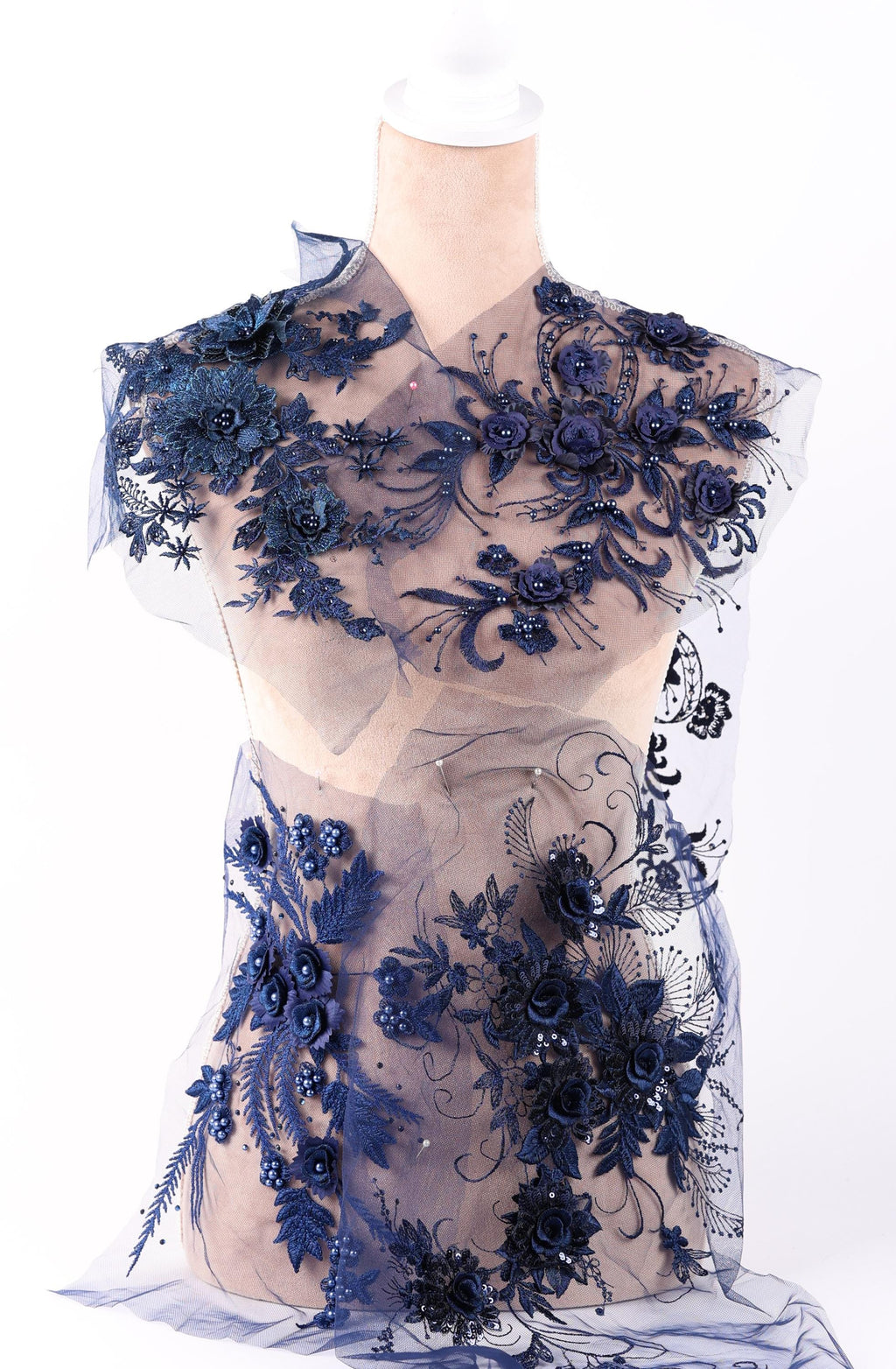 A mannequin wearing a dress with a sheer, lace-like fabric adorned with intricate floral and leaf designs in shades of blue.