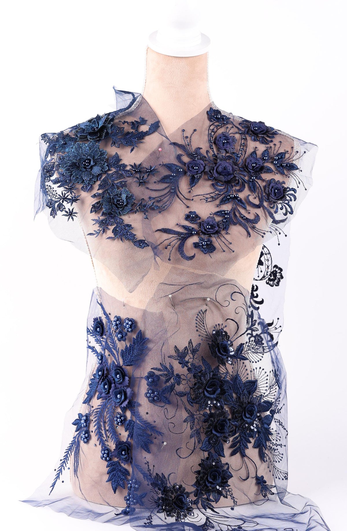 A mannequin wearing a dress with a sheer, lace-like fabric adorned with intricate floral and leaf designs in shades of blue.