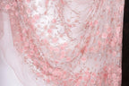 a close-up view of a delicate, pink floral fabric with numerous small pink roses and leaves. The fabric appears to be made of sheer material, giving it a soft and delicate appearance.