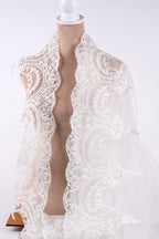 A mannequin wearing a white lace shawl with intricate floral patterns.