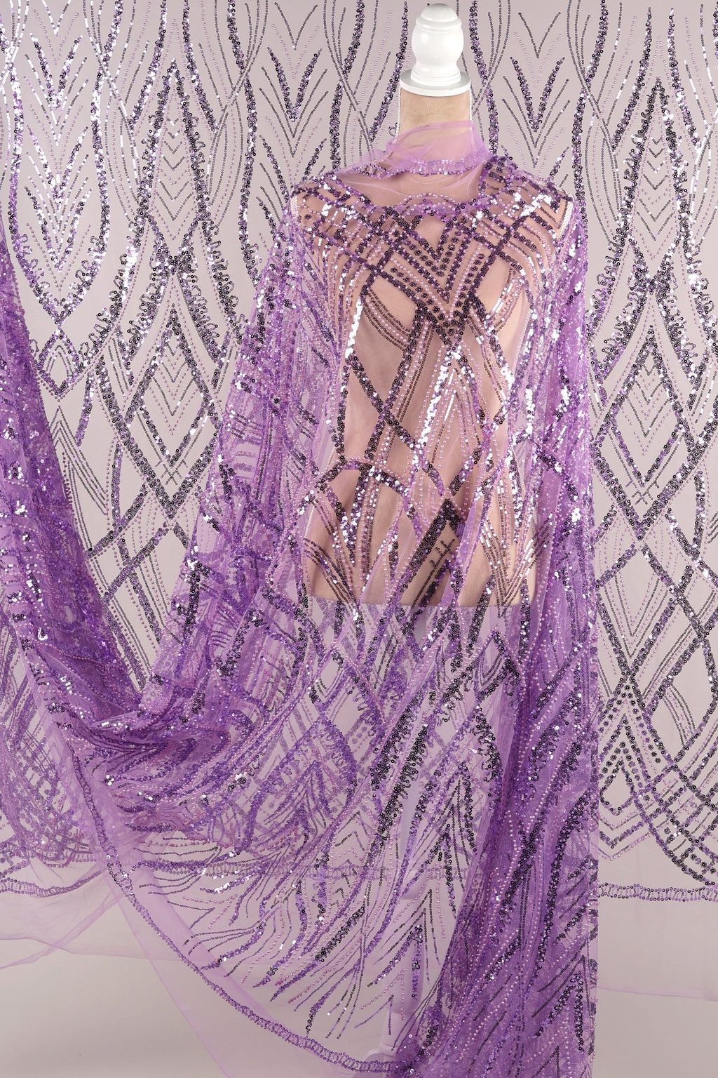 a mannequin wearing a purple sequin dress with a sheer overlay. The dress has a pattern of purple and silver sequins, creating a visually striking and elegant design.