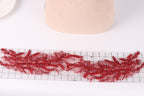 a close-up view of a piece of red embroidery with a floral pattern, placed on a ruler for scale.