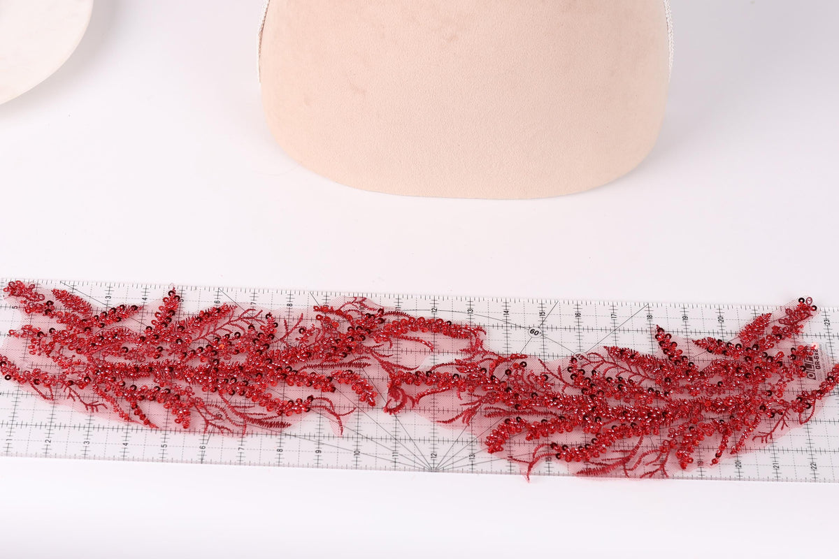 a close-up view of a piece of red embroidery with a floral pattern, placed on a ruler for scale.