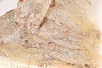 The image is a close-up of a fabric with a gold and beige color scheme, adorned with small gold and beige sequins and flowers.