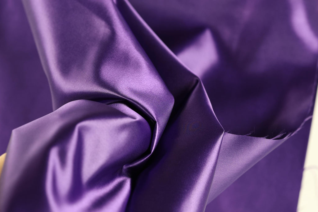 The image is a close-up of a purple fabric, possibly silk or satin, with a smooth and shiny texture.