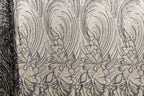 a close-up view of a fabric with a repeating floral pattern in shades of black and gold. The pattern consists of stylized flowers and leaves, creating a visually striking and intricate design. The fabric appears to be made of a shiny, metallic material, which adds a unique texture and visual interest to the overall composition.