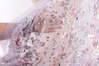 a close-up view of a delicate, intricately embroidered fabric with a floral pattern. The fabric appears to be made of sheer material, giving it a soft and delicate appearance. The embroidery features a variety of flowers and leaves in different colors, creating a visually appealing and detailed design. The fabric is being held by someone's hand, suggesting that it might be a piece of clothing or a decorative textile.