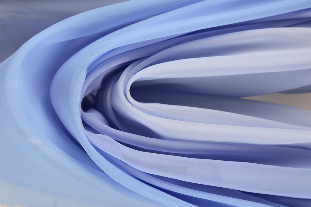 The image is a close-up of a fabric with a soft, flowing texture in shades of blue and white. The fabric appears to be made of silk or a similar material, and it is draped or folded in a way that creates a sense of movement and softness. The colors and texture of the fabric create a visually appealing and harmonious composition.
