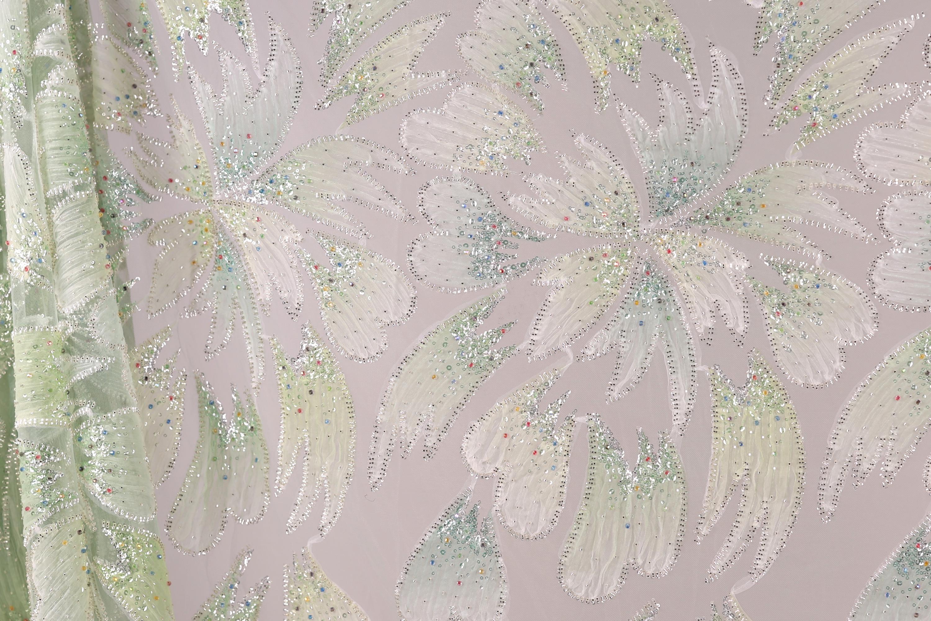 a close-up view of a fabric with a floral pattern, adorned with small, multicolored beads or sequins that create a sparkling effect.