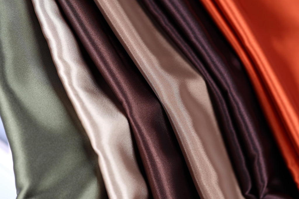 A close-up view of a collection of colorful satin fabric, with various shades of green, brown, and orange.