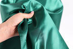 A hand is holding a piece of green satin fabric, with the fabric being folded and held in the palm of the hand.