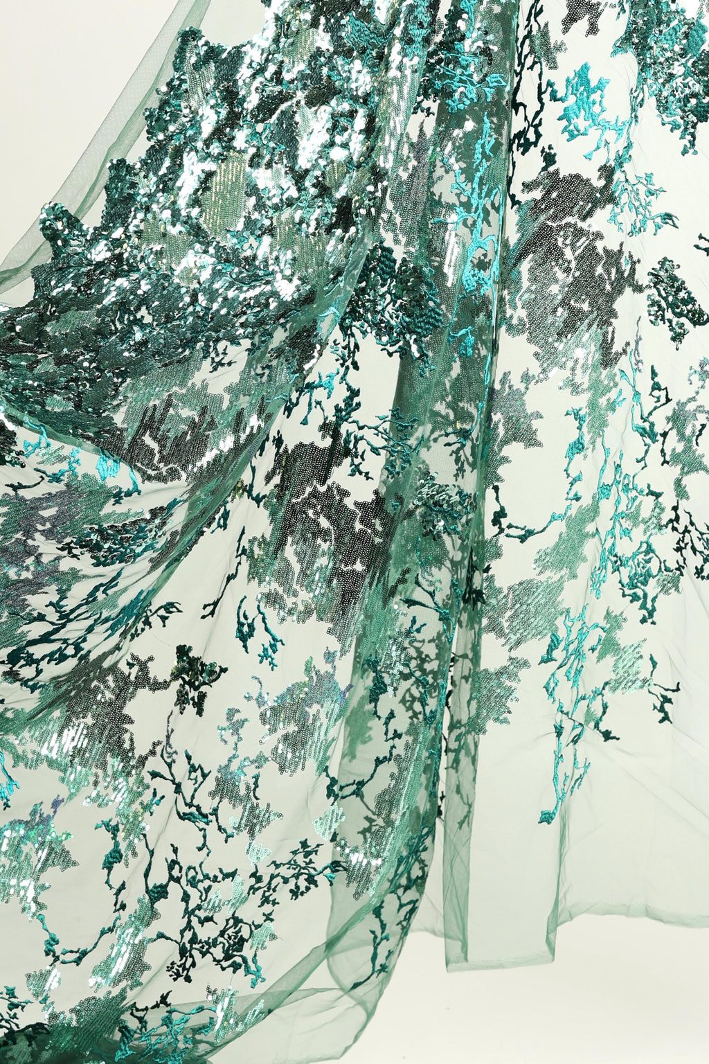 a close-up view of a fabric with a floral pattern in shades of green and blue. The fabric appears to be made of sheer material, with a textured and intricate design that resembles a lace or chiffon pattern. The colors and details of the fabric create a visually appealing and delicate appearance.
