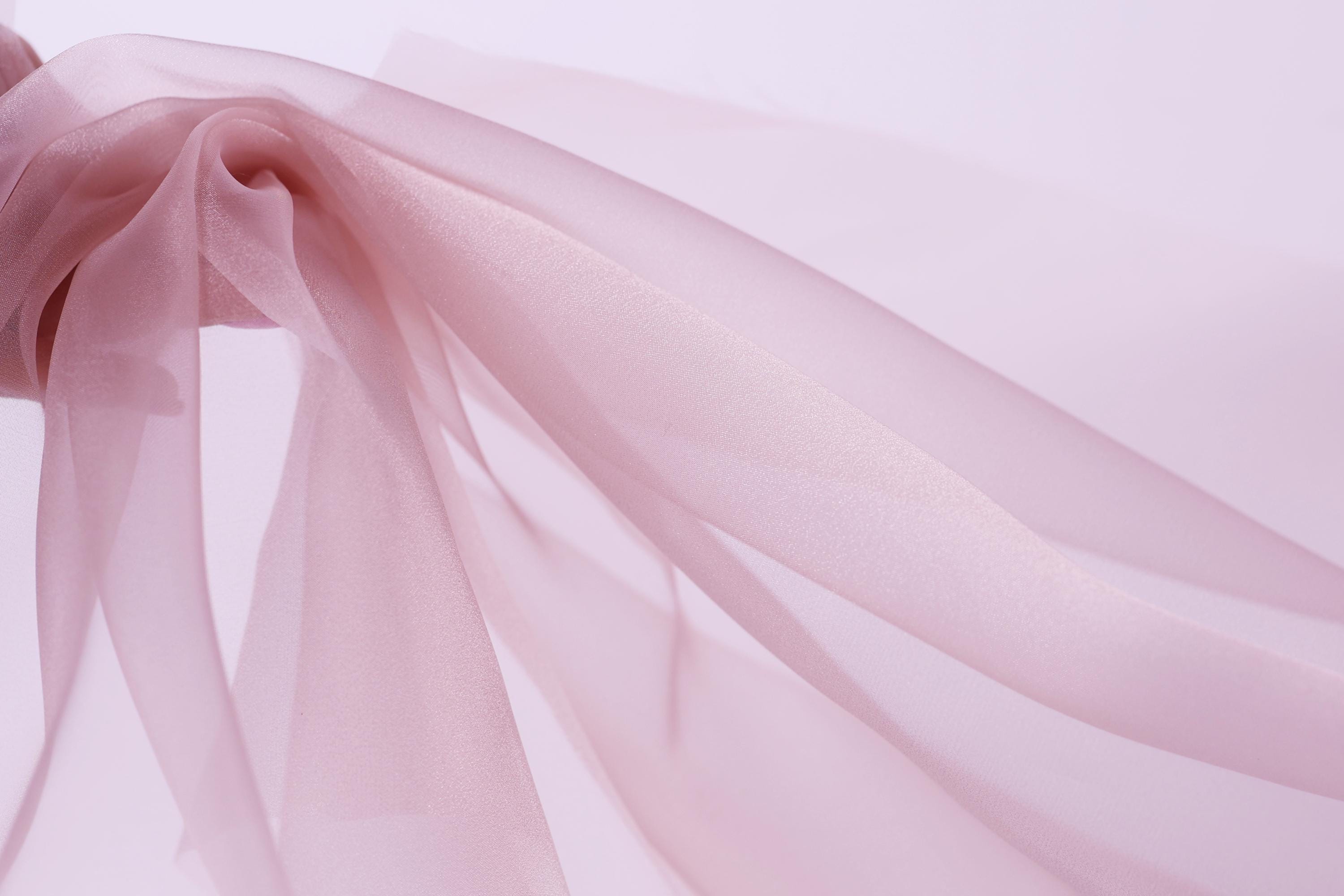 A close-up view of a delicate, flowing pink fabric, possibly silk or chiffon, with a soft, delicate texture.
