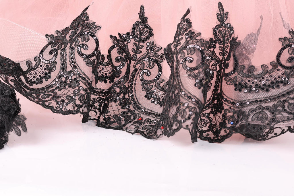 a close-up view of a delicate, lace-like fabric with intricate black embroidery and embellishments, including small red and blue accents.