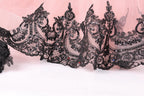 a close-up view of a delicate, lace-like fabric with intricate black embroidery and embellishments, including small red and blue accents.