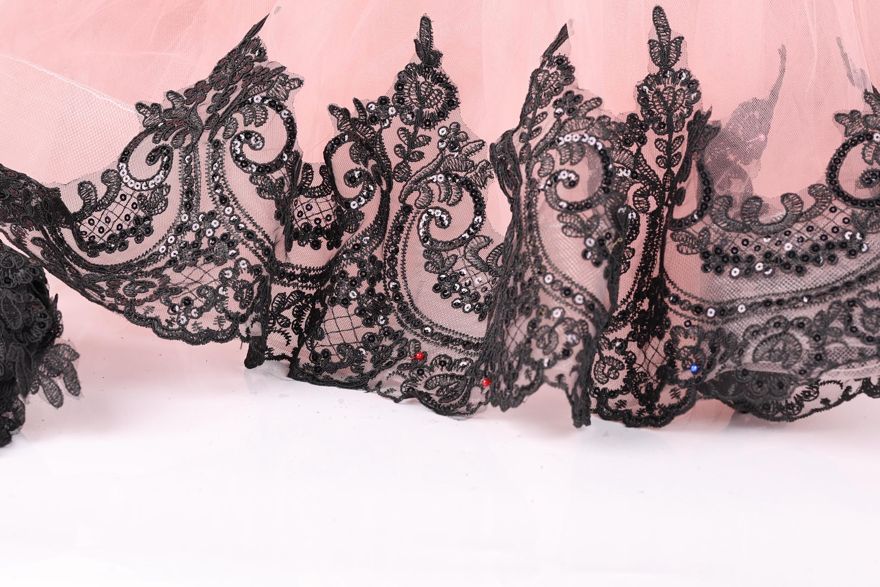 a close-up view of a delicate, lace-like fabric with intricate black embroidery and embellishments, including small red and blue accents.