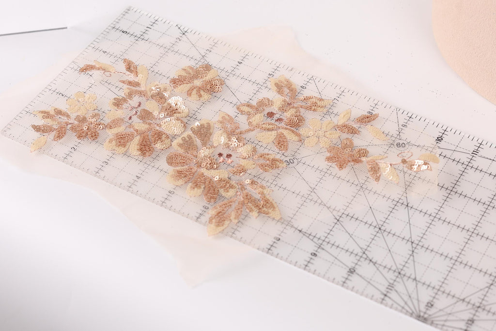 a close-up view of a clear ruler with a floral pattern of gold and beige sequins and leaves on it.