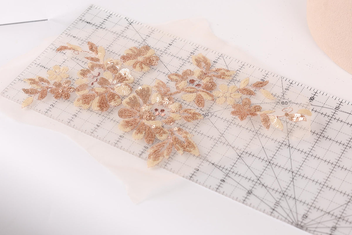a close-up view of a clear ruler with a floral pattern of gold and beige sequins and leaves on it.