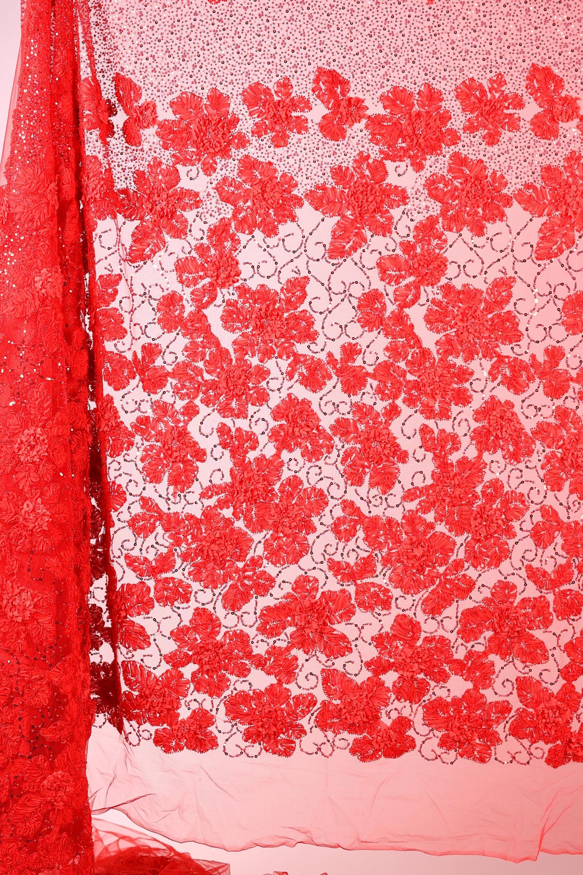 a close-up view of a red fabric with a floral pattern. The fabric appears to be made of a sheer material, with a repeating pattern of red flowers or leaves. The fabric is hanging on a surface, and the background is a light pink color. The image does not contain any text or other objects, and the focus is solely on the floral pattern on the fabric.