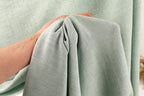 A hand is holding a piece of light green fabric, which appears to be a textile or fabric material.