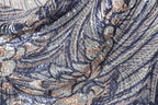 a close-up view of a fabric with a complex, intricate pattern of sequins and threads in shades of blue, silver, and gold. The fabric appears to be a piece of clothing or textile, with the intricate design and shimmering sequins creating a visually striking and detailed appearance.