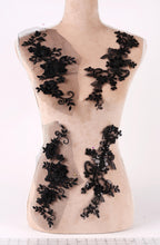 A mannequin torso with black lace appliques or decorations sewn onto it.