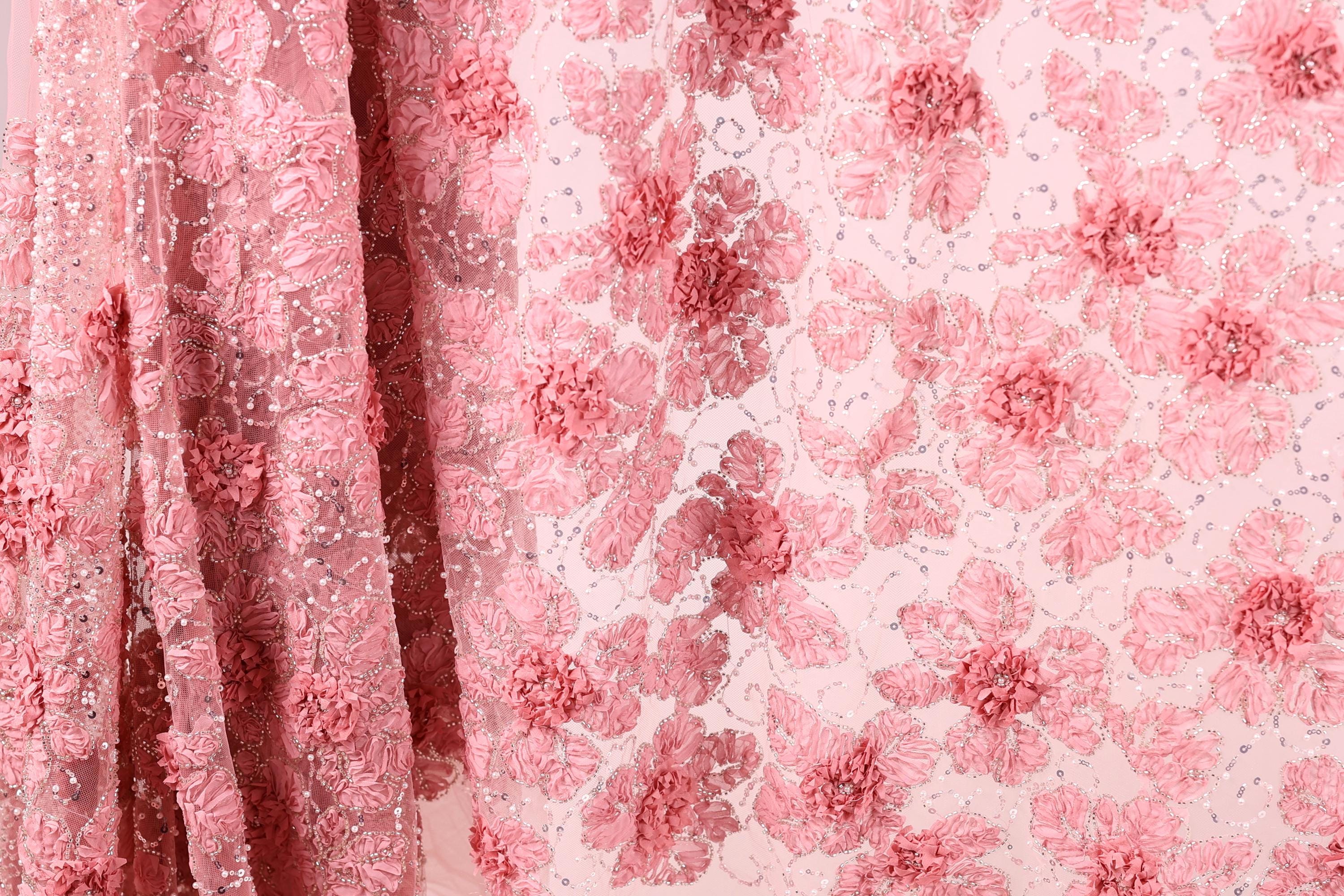 a close-up view of a fabric with a pink floral pattern. The fabric appears to be made of a sheer material, with a delicate and intricate design of pink flowers and leaves. The pattern is quite detailed and visually appealing, showcasing the craftsmanship and artistry involved in creating the fabric.