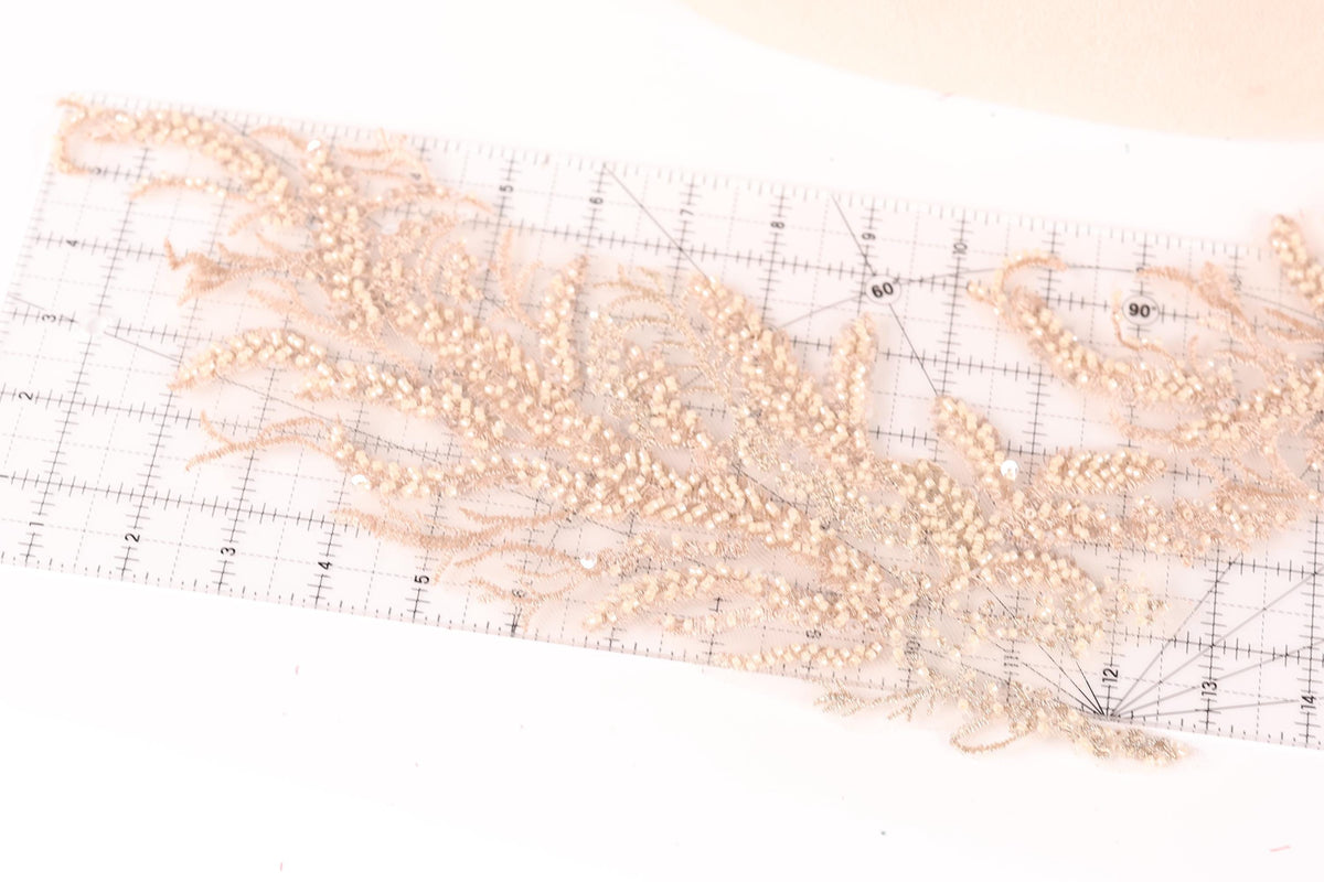 a close-up view of a delicate, intricate piece of embroidery or lace with numerous small, beige-colored beads or pearls attached to it. The beads are arranged in a way that they appear to be growing out of the fabric, creating a visually striking and detailed design.