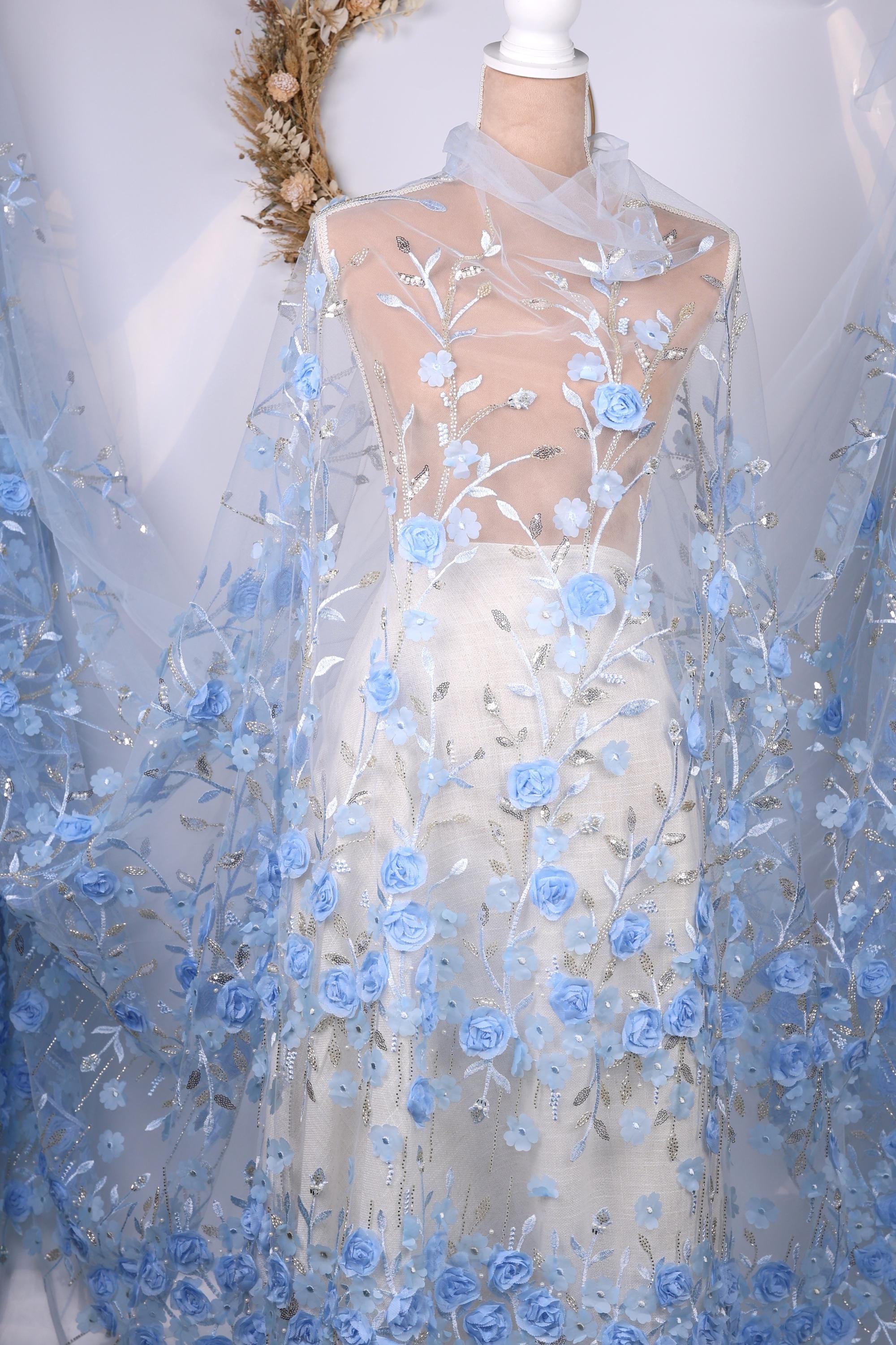 A mannequin wearing a white dress with a sheer blue floral fabric draped over it.