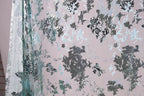 a close-up view of a fabric with a floral pattern in shades of blue and gray. The fabric appears to be made of a shiny, metallic material, giving it a textured and visually interesting appearance.