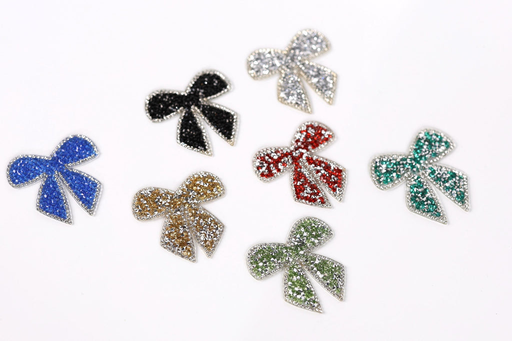 seven glittery bow-shaped objects in various colors, including blue, black, red, green, gold, and silver.