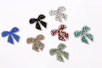 seven glittery bow-shaped objects in various colors, including blue, black, red, green, gold, and silver.