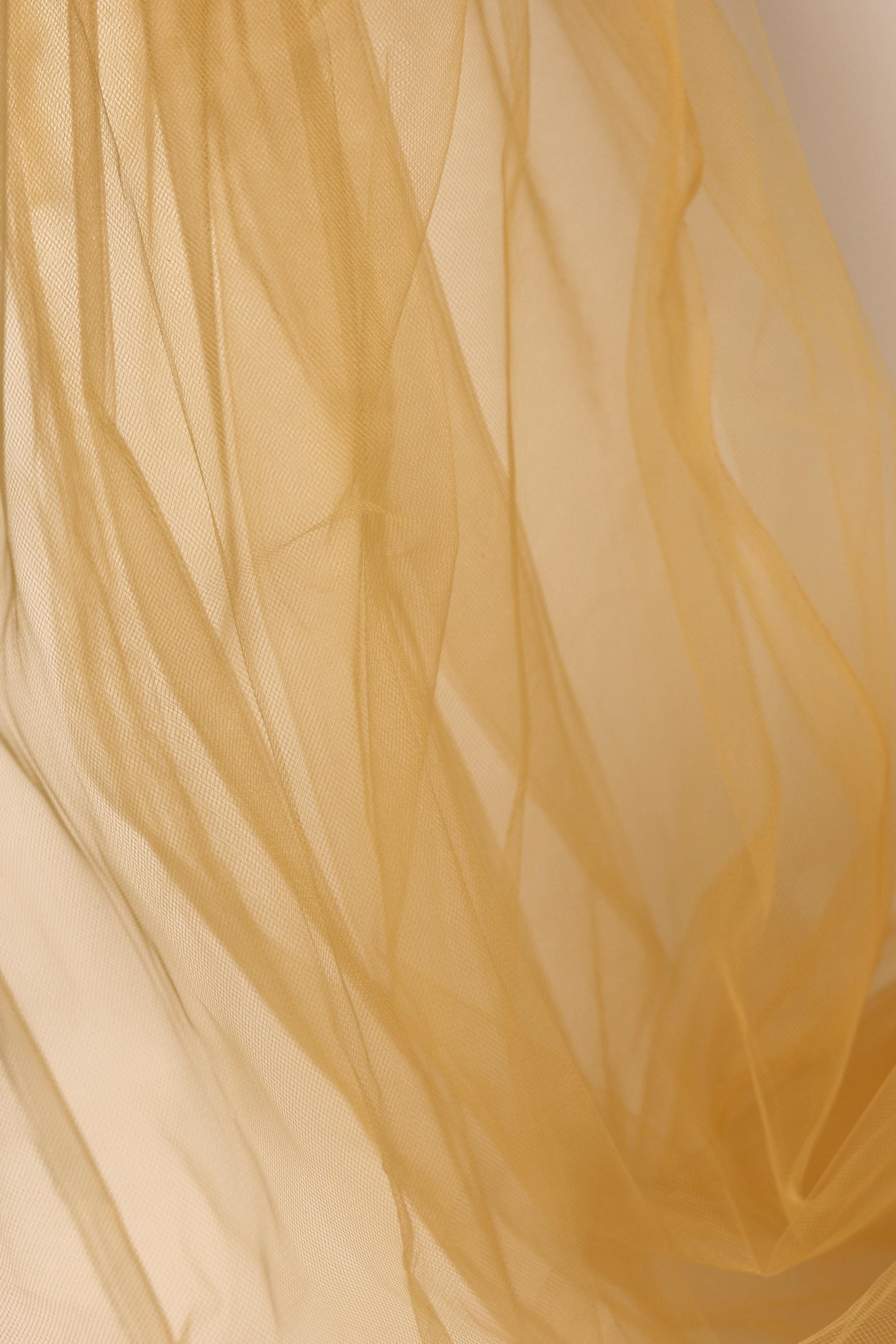The image is a close-up of a light brown, flowing fabric, possibly a sheer or sheer-like material, with a soft, delicate texture.