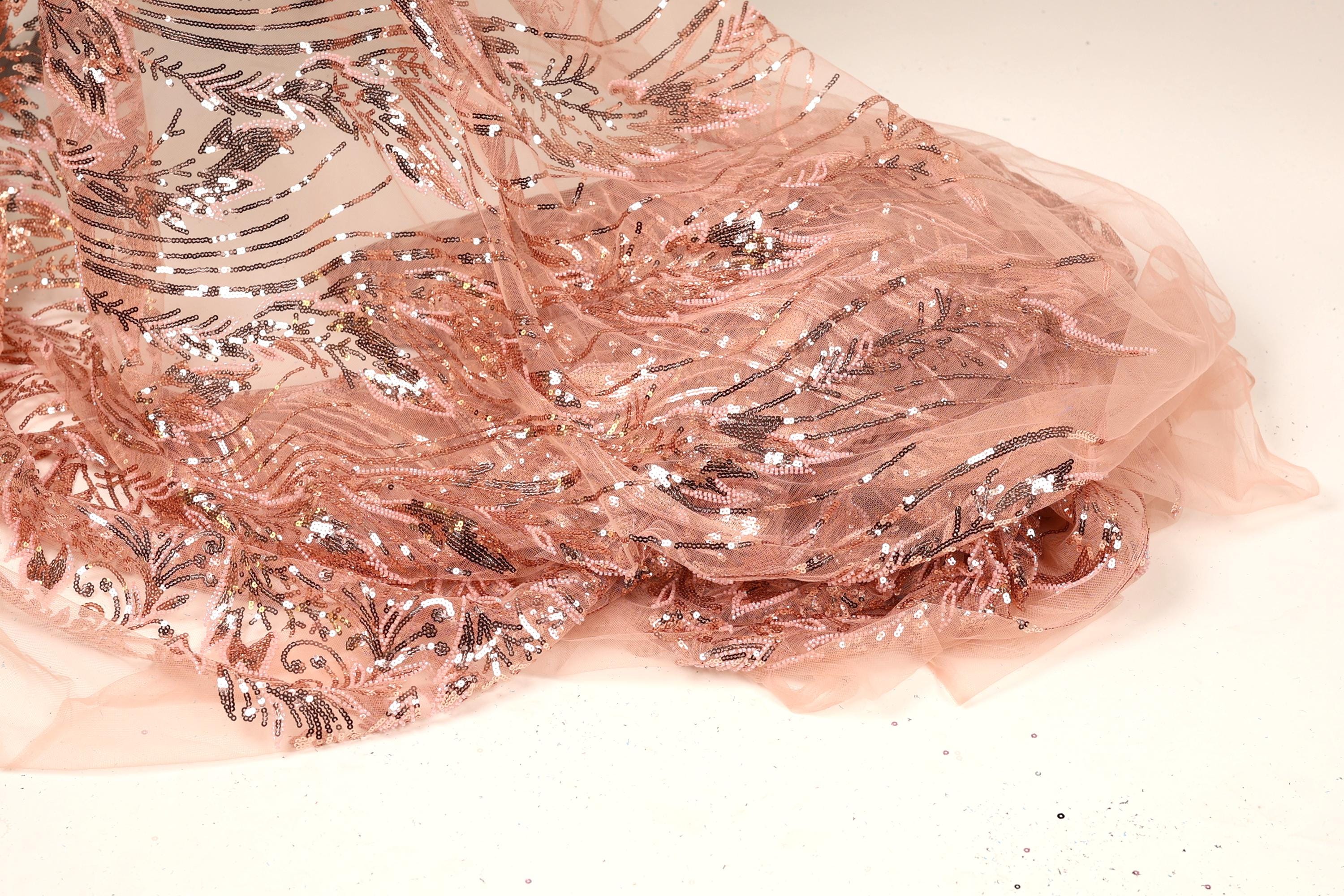 a close-up view of a delicate, pink sequined fabric with a floral pattern. The fabric appears to be made of sheer material, giving it a soft and delicate appearance.