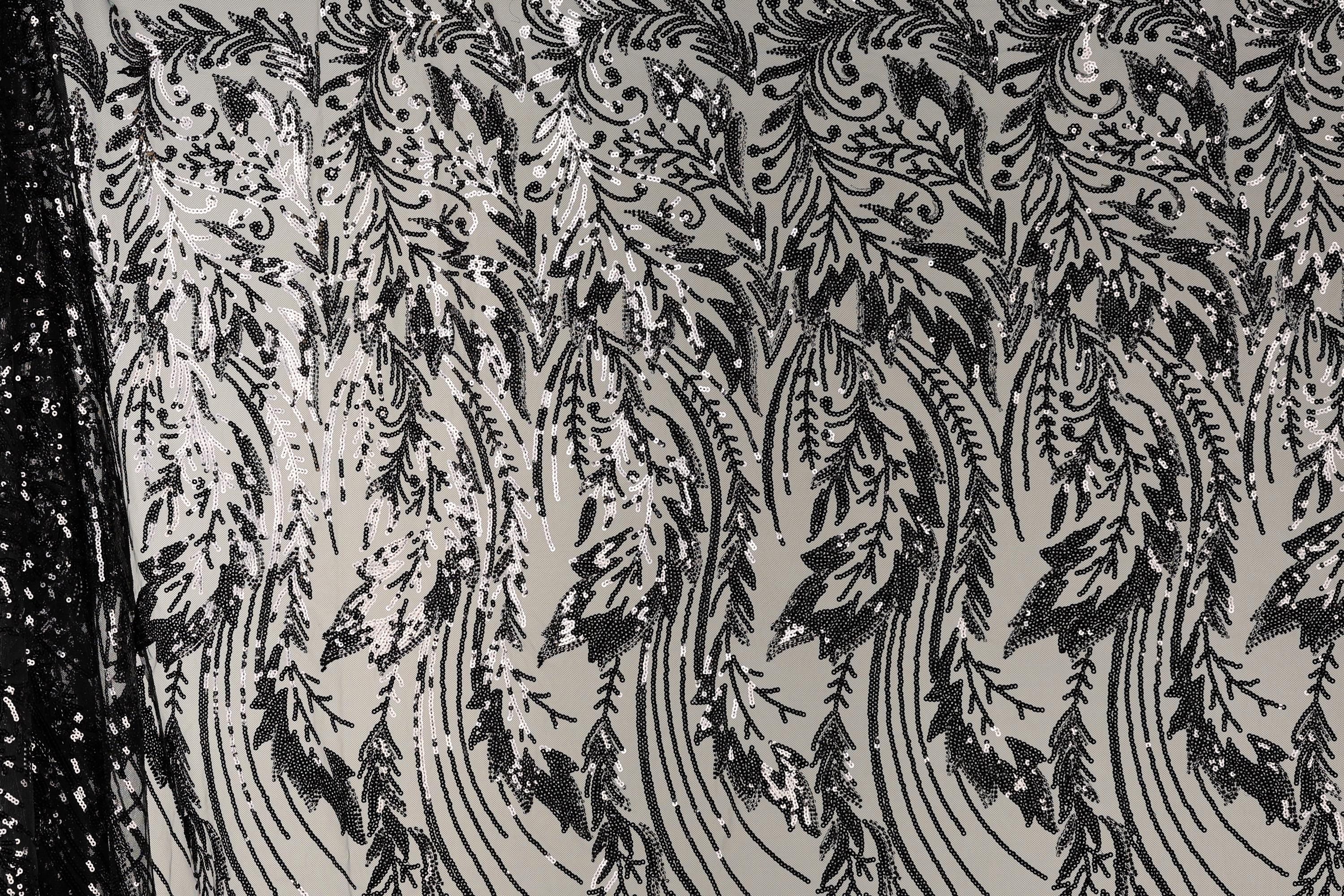 a close-up view of a fabric with a repeating pattern of black and white floral designs. The pattern consists of various shapes and lines, creating a visually striking and intricate design. The fabric appears to be made of a material with a metallic or sequined texture, adding a touch of sparkle and elegance to the overall appearance.