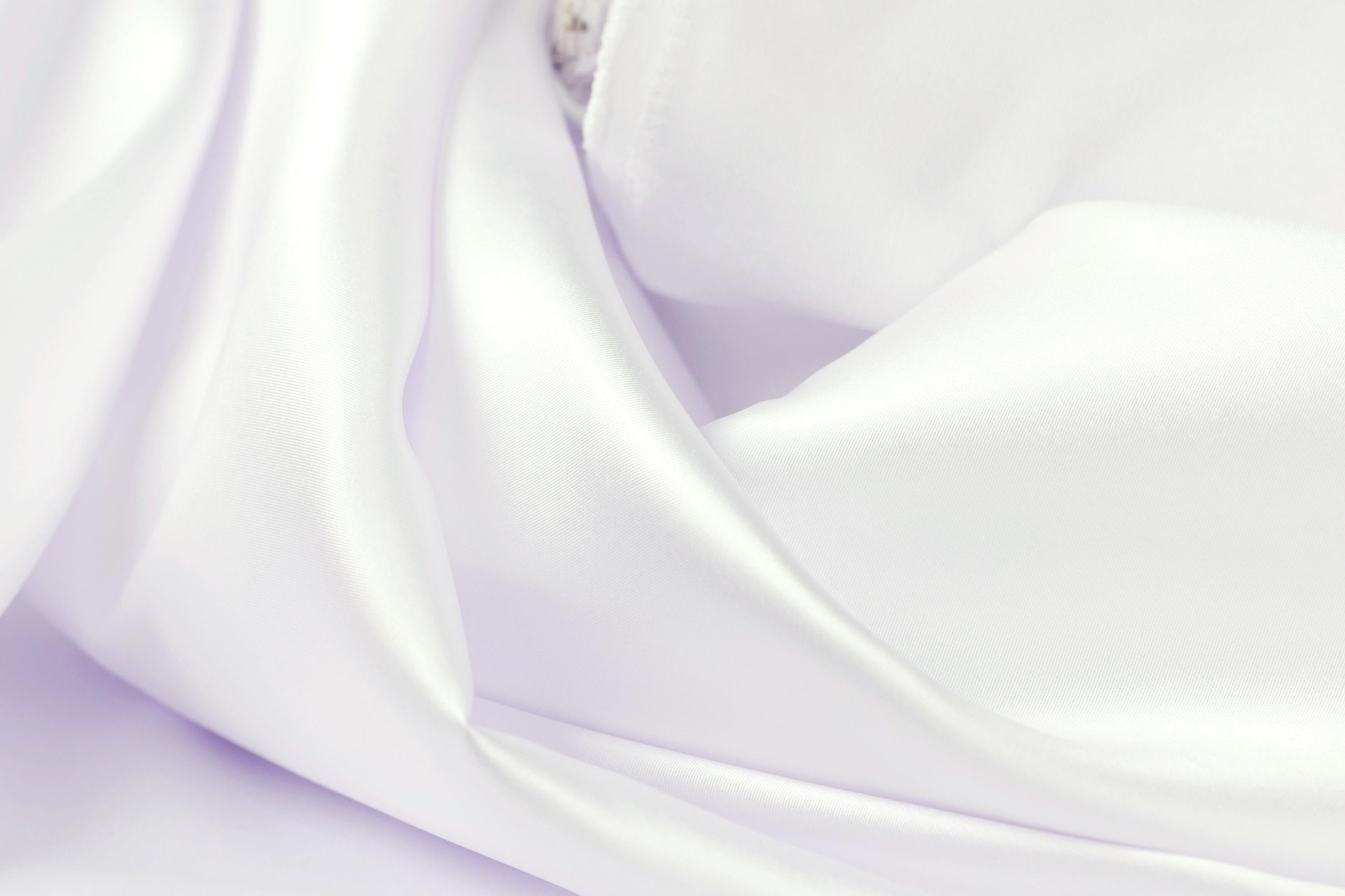 The image is a close-up of a soft, flowing white fabric, possibly a satin or chiffon material. The fabric appears to be wrinkled, giving it a delicate and elegant appearance.