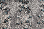 The image is a close-up of a fabric with a repeating pattern of blue and gray floral designs. The pattern consists of various shades of blue and gray flowers and leaves, creating a visually striking and intricate design. The fabric appears to be a textile or material with a textured surface, adding depth and dimension to the overall appearance.
