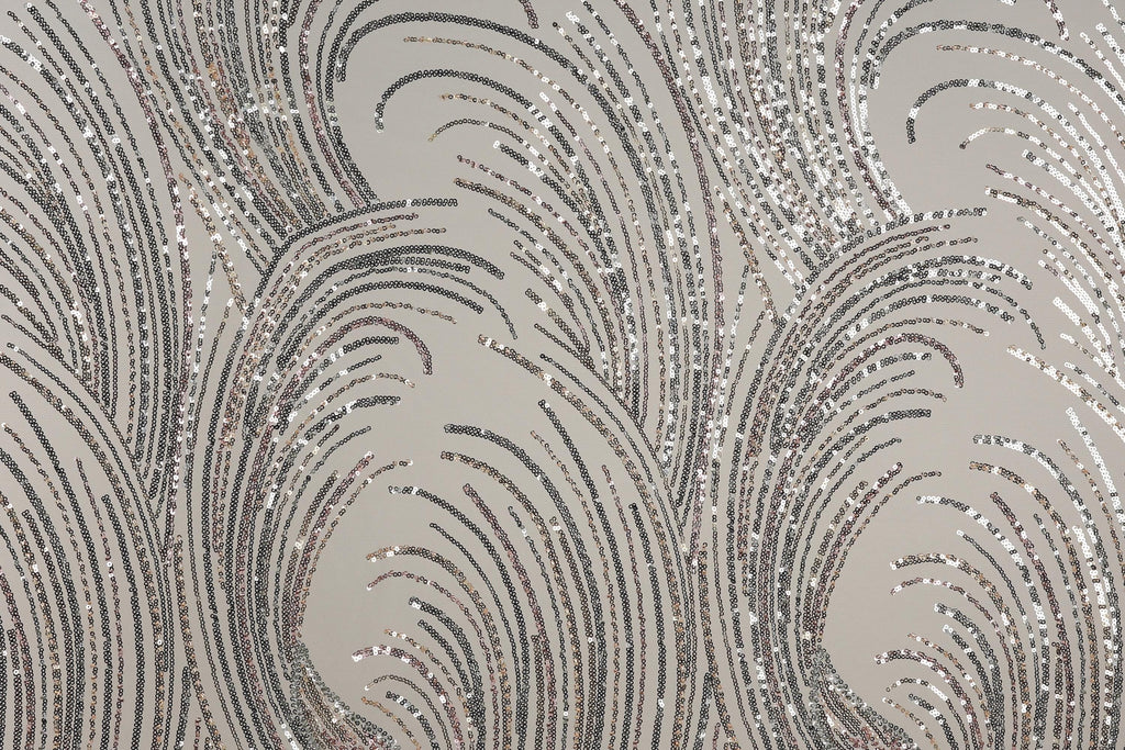 a close-up view of a fabric with a repeating pattern of silver and black sequin designs. The pattern consists of curved lines and swirls, creating a visually striking and intricate design. The fabric appears to be a light-colored material, possibly a type of lace or a similar decorative textile.