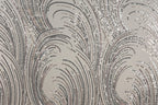 a close-up view of a fabric with a repeating pattern of silver and black sequin designs. The pattern consists of curved lines and swirls, creating a visually striking and intricate design. The fabric appears to be a light-colored material, possibly a type of lace or a similar decorative textile.