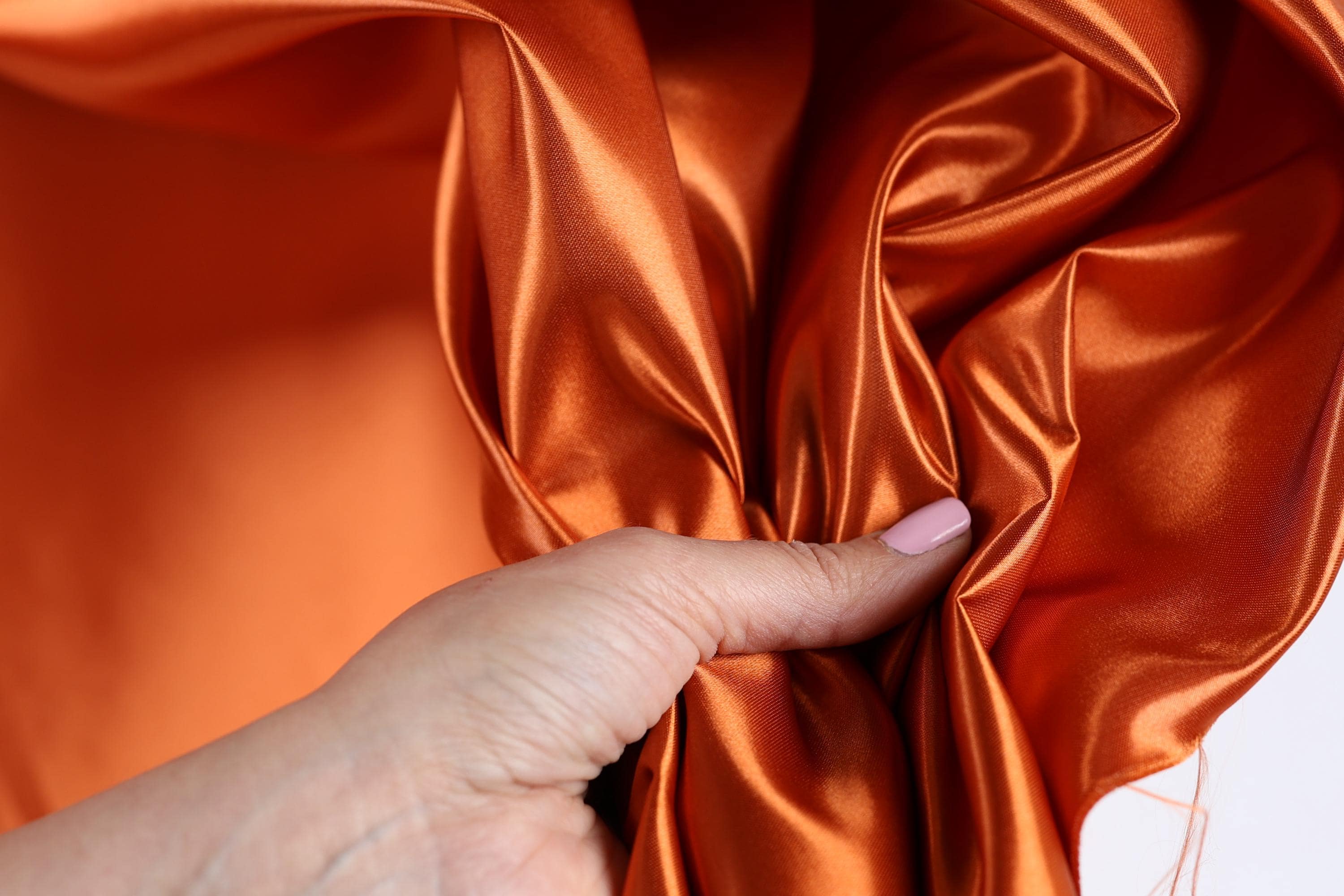 A hand is holding a piece of orange satin fabric, with the fabric's folds and creases visible.