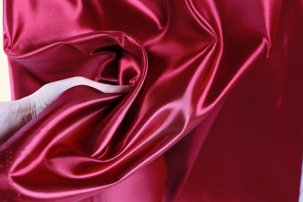 A hand is holding a piece of red satin fabric, which appears to be a close-up view of the material.