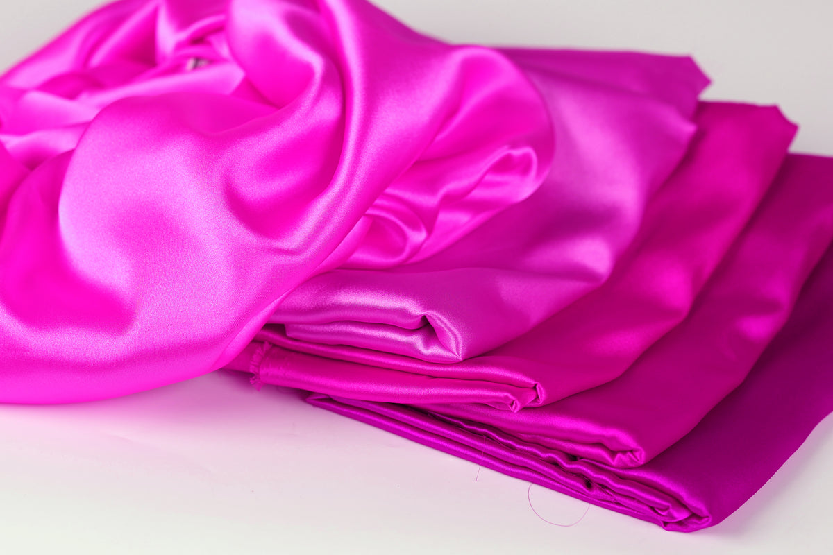 A pile of shiny, vibrant pink satin fabric is displayed against a white background.